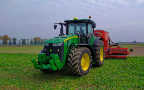 Na zdjęciu zielony ciągnik marki John Deer z siewnikiem rzędowym Kuhn Aurock 6000 RC podczas siewu